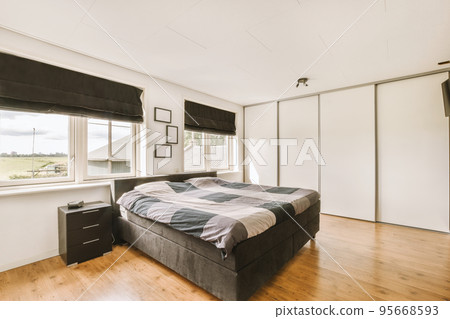 Home interior design of bedroom with bed and wooden wardrobe placed in corner near window in modern apartment 95668593
