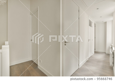 Perspective view of empty narrow hallway with white walls and wardrobe with mirror and parquet floor in minimalist style apartment 95668746