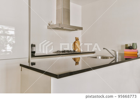 Fragment of interior of light narrow home kitchen with minimalist style white furniture with sink and stove Fragment of interior of light narrow home kitchen with minimalist style white furniture with sink and stove 95668773