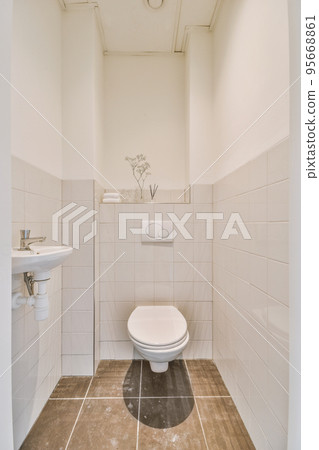 Wall hung toilet and small sink in corner in lavatory room with beige tile 95668861