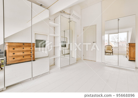 Modern cupboard and vintage chest placed near doors and wicker basket in spacious room with white walls and wooden floor 95668896