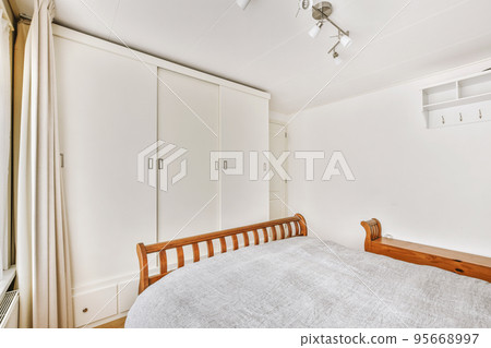 Home interior design of bedroom with bed and wooden wardrobe placed in corner near window in modern apartment Home interior design of bedroom with bed and wooden wardrobe placed in corner near window in modern apartment 95668997