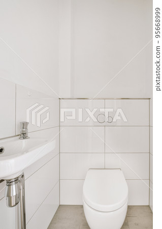 Interior of narrow restroom with sink and wall hung toilet with white walls and checkered floor Interior of narrow restroom with sink and wall hung toilet with white walls and checkered floor 95668999