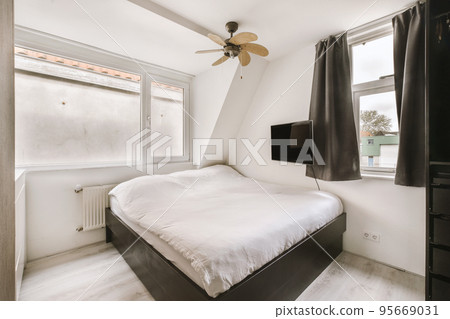 Minimalist interior design of small bedroom with soft bed placed in corner and wooden wardrobe and shelves with lamp illumination Minimalist interior design of small bedroom with soft bed placed in corner and wooden wardrobe and shelves with lamp illumination 95669031