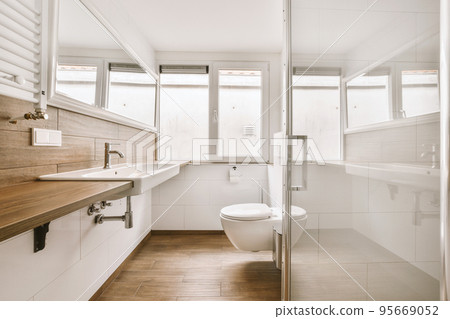 Modern flush toilet and ceramic sink installed on white tiled walls near mirror and towel in small restroom at home Modern flush toilet and ceramic sink installed on white tiled walls near mirror and towel in small restroom at home 95669052