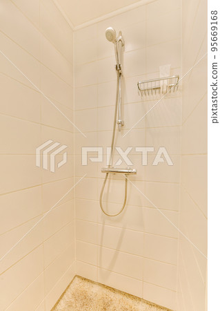 Shower faucets attached to tiled wall near glass partition and ornamental curtail in washroom at home 95669168