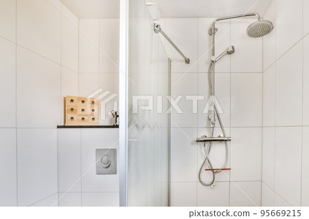 Shower faucets attached to tiled wall near glass partition and ornamental curtail in washroom at home 95669215