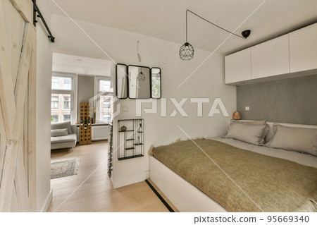 Comfortable bed located near window with blinds in light bedroom of contemporary flat 95669340