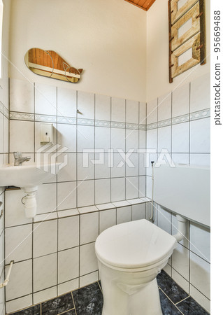 Wall hung toilet and small sink in corner in lavatory room with beige tile Wall hung toilet and small sink in corner in lavatory room with beige tile 95669488