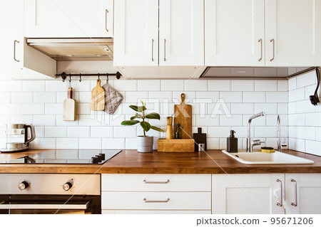 Kitchen brass utensils, chef accessories. Hanging kitchen with white tiles wall and wood tabletop.Green plant on kitchen background  95671206