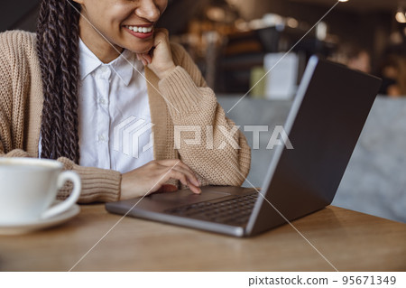 Cropped view to a cute ethnic woman smiling toothy smile while working on laptop during coffee break inside a cafeteria 95671349