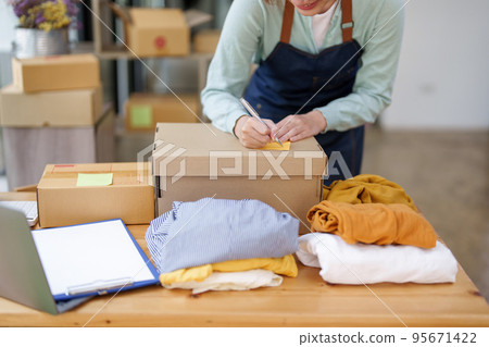 A portrait of a small startup, and SME owner, an Asian female entrepreneur, is writing down information on a notepad to organize the product before packing it into the inner box for the customer. A portrait of a small startup, and SME owner, an Asian female entrepreneur, is writing down information on a notepad to organize the product before packing it into the inner box for the customer. 95671422