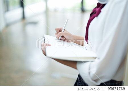 Portrait of a beautiful young Asian student using a notebook to take notes in the library. Portrait of a beautiful young Asian student using a notebook to take notes in the library. 95671789