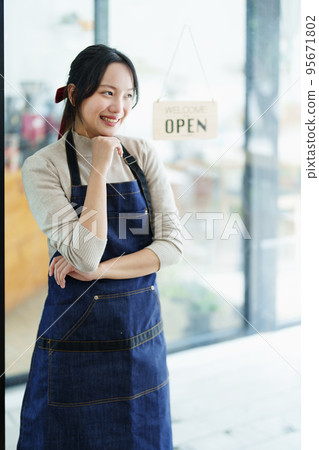 Starting and opening a small business, a young Asian woman showing a smiling face in an apron standing in front of a coffee shop bar counter. Business Owner, Restaurant, Barista, Cafe, Online SME. Starting and opening a small business, a young Asian woman showing a smiling face in an apron standing in front of a coffee shop bar counter. Business Owner, Restaurant, Barista, Cafe, Online SME. 95671802