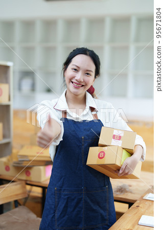 Starting small business entrepreneur of independent Asian woman smiling using computer laptop with cheerful success of online marketing package box items and SME delivery concept. 95671804
