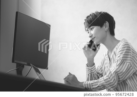 A woman working on a computer while talking on her smartphone monochrome 95672428