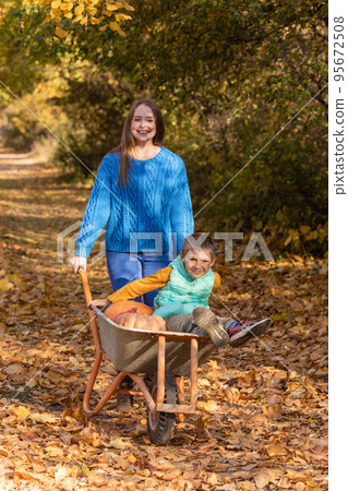 Mother have fun time with kid, use garden wheelbarrow with pumpkins Mother have fun time with kid, use garden wheelbarrow with pumpkins 95672508