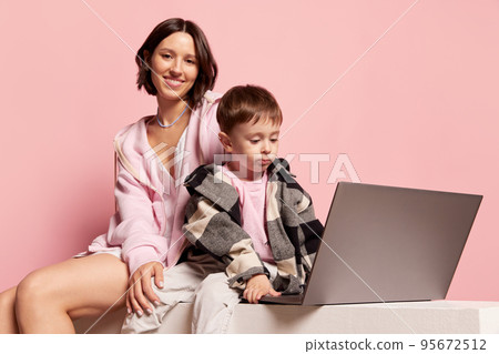 Educational games. Young woman and little boy, mom and son using laptop isolated on pink studio background. Mother's Day celebration. Concept of family, childhood, motherhood 95672512