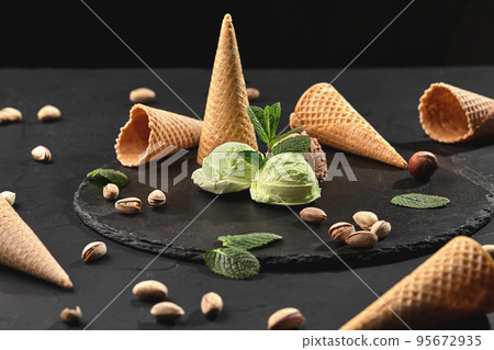 Gourmet chocolate and pistachio ice cream served on a stone slate over a black background. 95672935