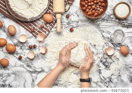 Close-up shot. Top view of a baker cook place, hands are working with a raw dough on the marble table background. Close-up shot. Top view of a baker cook place, hands are working with a raw dough on the marble table background. 95673023