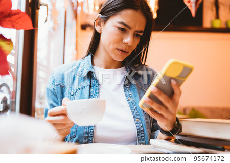 Concerned young woman reading bad news on her smartphone Concerned young woman reading bad news on her smartphone 95674172