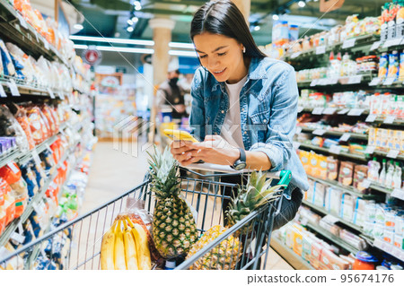 Happy young woman shopping for groceries in supermarket Happy young woman shopping for groceries in supermarket 95674176