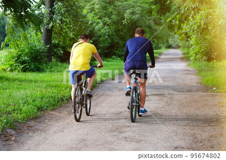 Cyclists spend their time on bicycles  in park on sunny day among many trees. Ride for exercise and relaxation. Healthy lifestyle. Sport and active life concept. 95674802