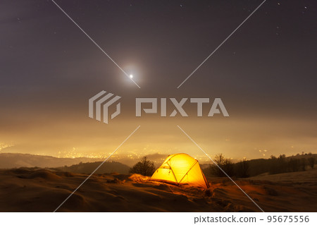 Yellow tent lighted from the inside against the backdrop of glowing city lights 95675556