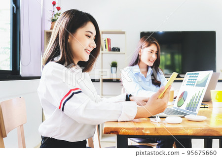 A female employee uses a phone and computer to check the company's investment budget A female employee uses a phone and computer to check the company's investment budget 95675660