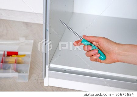 Repairs in house or apartment. Female hand repairing white furniture with a screwdriver in home, close up. Do it yourself. Repairs in house or apartment. Female hand repairing white furniture with a screwdriver in home, close up. Do it yourself. 95675684