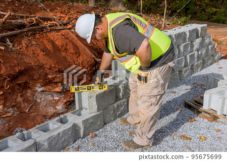 Contractor during installation of new large block retaining wall in construction site 95675699