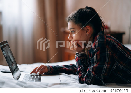 Young woman work while with laptop lying on bed Young woman work while with laptop lying on bed 95676455