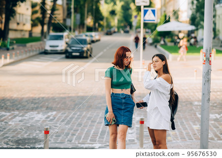 Two tourist friends consulting an online guide on a smart phone in the street Two tourist friends consulting an online guide on a smart phone in the street 95676530