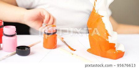 a little girl paints a toy fox made of clay. DIY concept 95676613