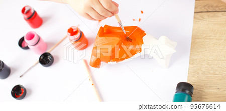a little girl paints a toy fox made of clay. DIY concept 95676614