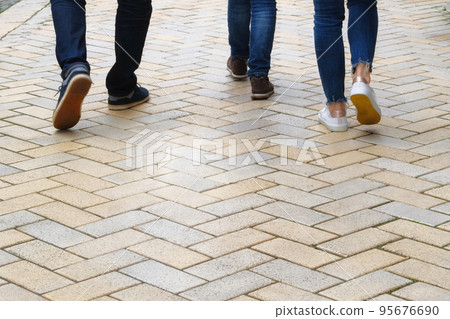 People walk along footpath. Yellow Paving slab. Pedestrian zone in the park in daylight, background. Urban walkway. People walk along footpath. Yellow Paving slab. Pedestrian zone in the park in daylight, background. Urban walkway. 95676690