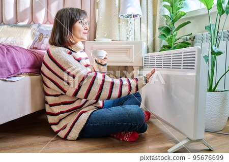 Woman warming herself in bedroom near electric heater 95676699
