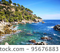 Panoramic photo of the rocky seashore with the sky, with green plants, trees and private houses. The Spanish coast of the Costa Brava, the Mediterranean Sea. Tourism, living in a beautiful place. 95676883