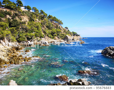 Panoramic photo of the rocky seashore with the sky, with green plants, trees and private houses. The Spanish coast of the Costa Brava, the Mediterranean Sea. Tourism, living in a beautiful place. 95676883