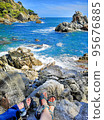 Panoramic photo of the rocky seashore with the feet of tourists in sandals, women and men. The concept of hiking ordinary people along the coast. 95676885