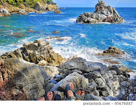 Panoramic photo of the rocky seashore with the feet of tourists in sandals, women and men. The concept of hiking ordinary people along the coast. 95676887