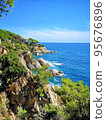 Panoramic photo of the rocky seashore with the sky, with green plants, trees and private houses. The Spanish coast of the Costa Brava, the Mediterranean Sea. Tourism, living in a beautiful place. 95676896
