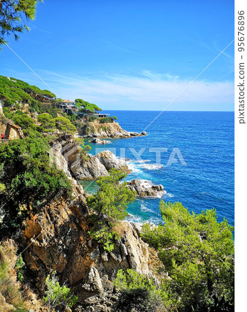 Panoramic photo of the rocky seashore with the sky, with green plants, trees and private houses. The Spanish coast of the Costa Brava, the Mediterranean Sea. Tourism, living in a beautiful place. Panoramic photo of the rocky seashore with the sky, with green plants, trees and private houses. The Spanish coast of the Costa Brava, the Mediterranean Sea. Tourism, living in a beautiful place. 95676896
