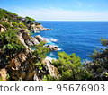Panoramic photo of the rocky seashore with the sky, with green plants, trees and private houses. The Spanish coast of the Costa Brava, the Mediterranean Sea. Tourism, living in a beautiful place. 95676903