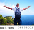 Panoramic photo of a happy man with outstretched arms, who conquered the peak of life with a beautiful view of the sea and the rocky shore. The concept of travel and freedom. 95676908