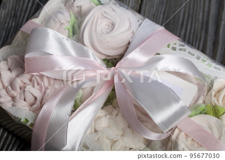 Homemade marshmallows in a gift box. Tied with ribbon. Zephyr flowers. On black pine boards. Taken from above. 95677030