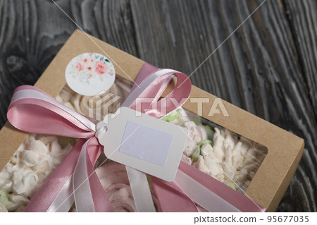 Homemade marshmallows in a gift box. Tied with ribbon. Zephyr flowers. On black pine boards. Taken from above. Homemade marshmallows in a gift box. Tied with ribbon. Zephyr flowers. On black pine boards. Taken from above. 95677035