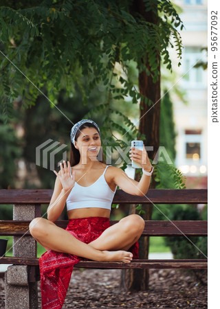 Woman using a smartphone in park sitting on a bench Woman using a smartphone in park sitting on a bench 95677092