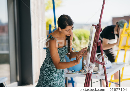 Young woman artist paints with a spatula on the canvas Young woman artist paints with a spatula on the canvas 95677104