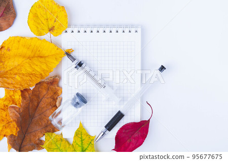 Vaccine and syringe are on table next to doctor's notebook and autumn leaves. Blank notebook for notes in doctor's office. Autumn vaccination. Vaccine and syringe are on table next to doctor's notebook and autumn leaves. Blank notebook for notes in doctor's office. Autumn vaccination. 95677675
